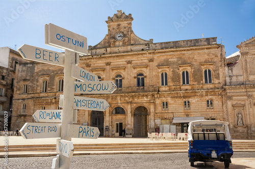 Canvastavla Tourist signpost with distances and in the background the Municipality of Ostuni