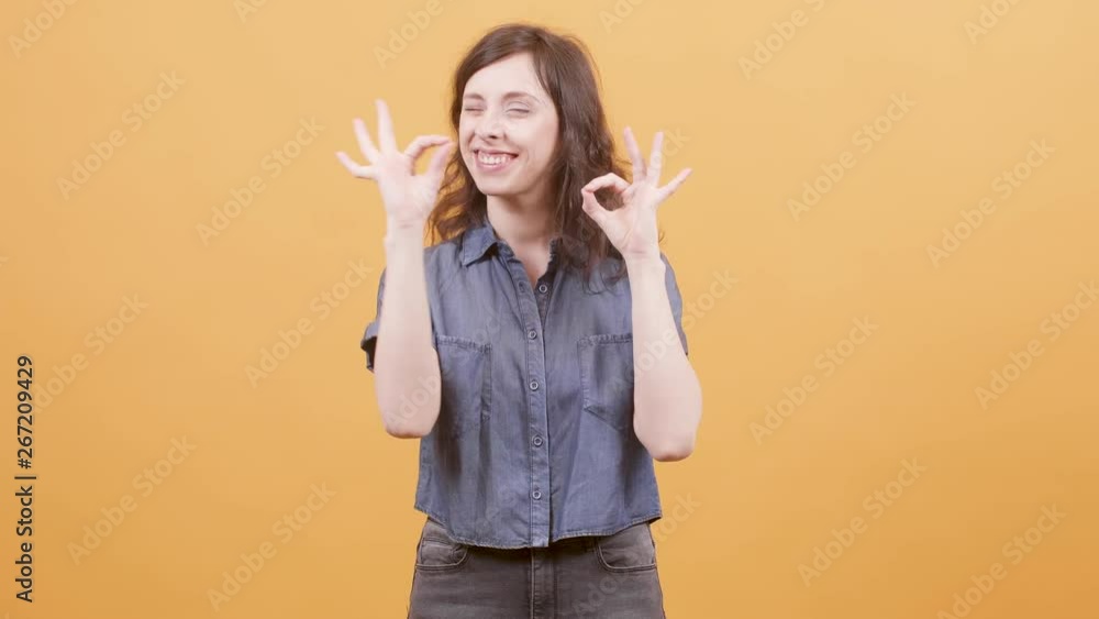 Pretty young woman showing ok sign as approval for a great job. Portrait of a female over yellow background. Pretty young woman showing ok sign as approval for a great job. Portrait of a female over yellow background.