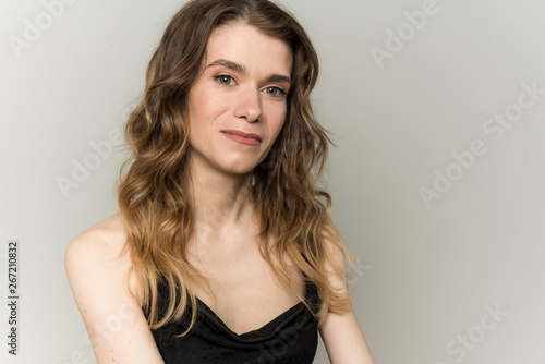 a portrait of the emotional young, sympathetic, sexy, European girl with a loose, loose hair who gently smiles and fixes her hair. On a light background