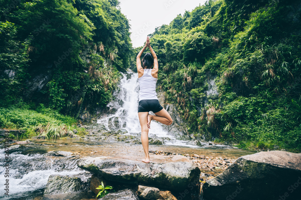 Young woman practice yoga near waterfall in forest