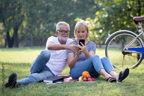 Happy senior couple relaxing in park using smartphone together . old people sitting on grass in the summer park looking mobile phone . Elderly resting .mature relationships