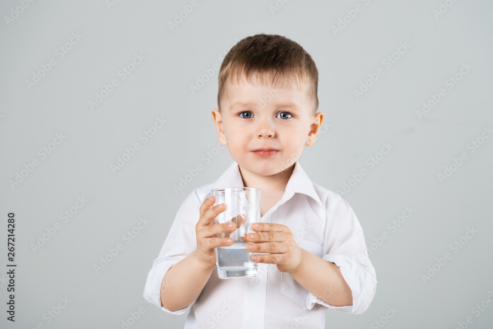Little boy drinking water from glass on gray background Little boy drinking water from glass on gray background