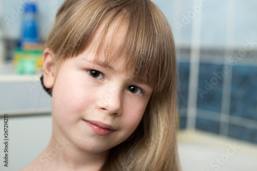 Pretty girl face portrait, child with beautiful eyes and long wet fair hair on blurred background of bathroom.