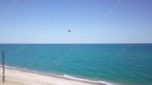Aquilone colorato che vola in spiaggia con sfondo del mare blu.