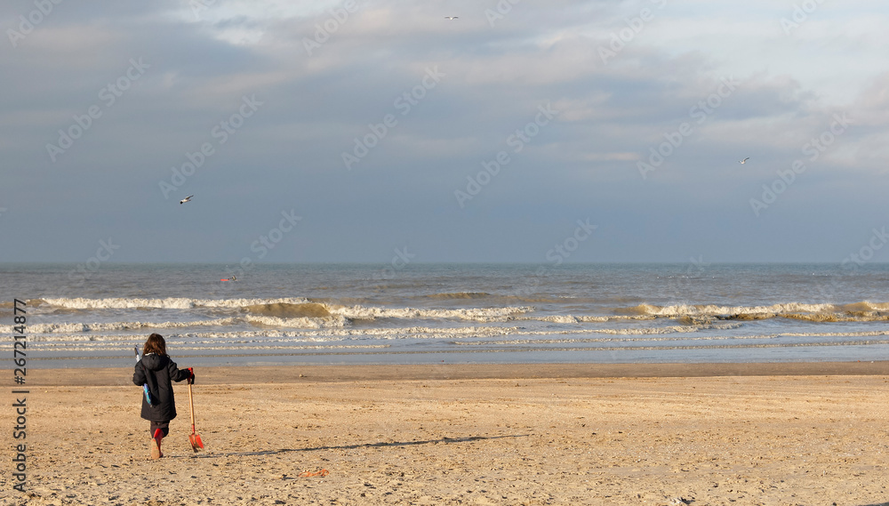 Little girl walking towards the sea on an empty beach in winter