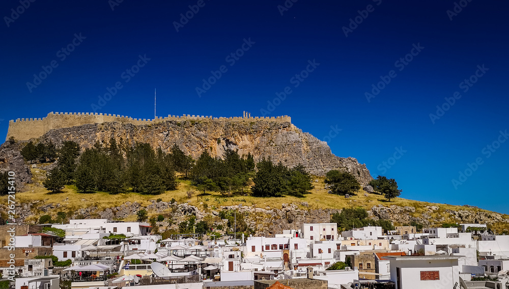 Lindos ,Rhodes/Greece May 2 2019 :the white houses in the historic village and the acropolis in the top of the mountain. view from terrace