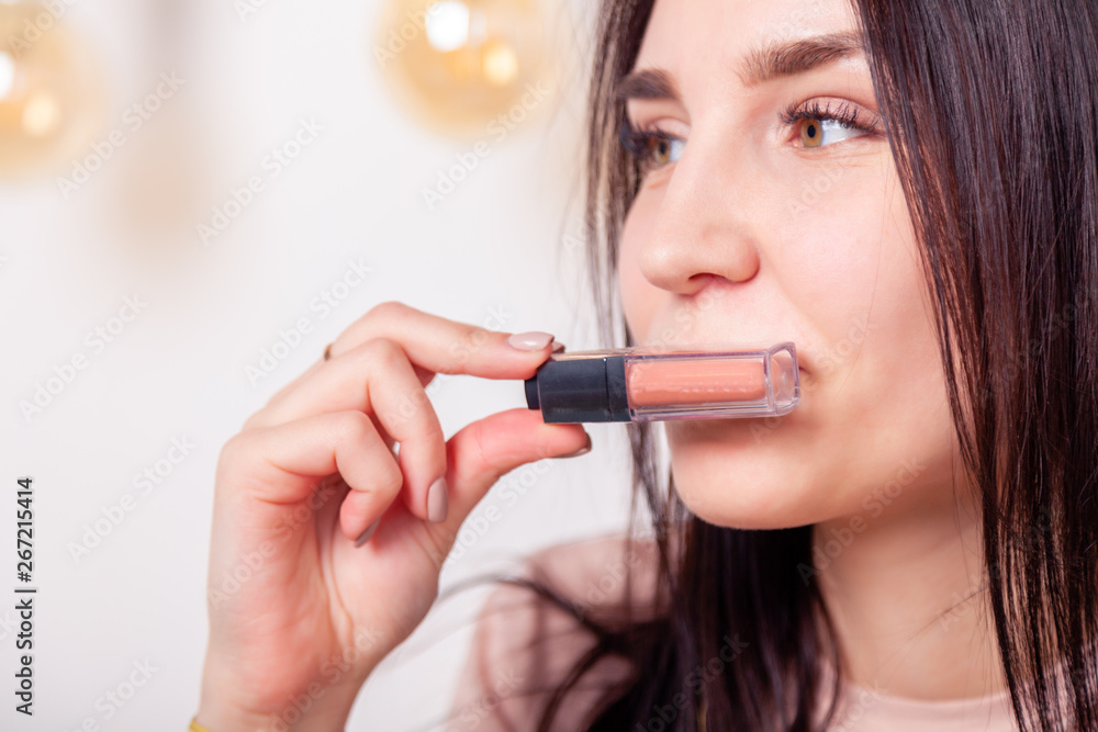 Beautiful caucasian girl make up artist, visagiste, model holding pastel beige liquid lipstick, lip gloss. Concept advertising no brand decorative professional cosmetic store Beautiful caucasian girl make up artist, visagiste, model holding pastel beige liquid lipstick, lip gloss. Concept advertising no brand decorative professional cosmetic store