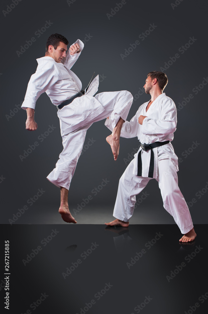 Handsome young male karate player doing kick on the gray background Handsome young male karate player doing kick on the gray background