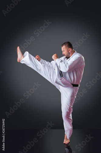 Handsome male karate player doing kick on the gray background