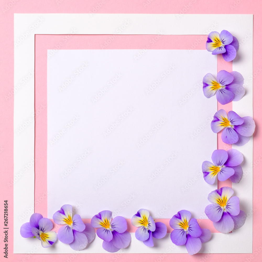 Creative flat lay composition: paper frame and blooming flowers petals on pink background. Top view, floral frame, abstract design. Invitation, greeting card or an element for your design