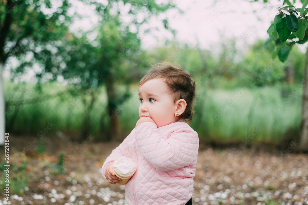 little girl in the garden on the background of greenery and trees very cute eating ice cream finger in a waffle Cup little girl in the garden on the background of greenery and trees very cute eating ice cream finger in a waffle Cup