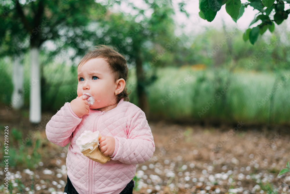 little girl in the garden on the background of greenery and trees very cute eating ice cream finger in a waffle Cup