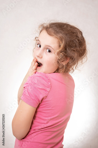 Close up portrait of a cute emotions little girl of 8 years old with curly hair, grey background