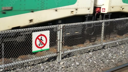Warning sign on railway for no crossing the tracks. A sign to warn people do not cross, no crossing the train tracks, with a train moving behind it. A sign warning for danger, with GO train moving 