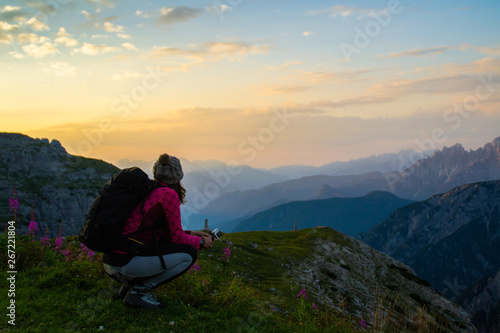 Hiker tourist woman overlooking rising sun and breathtaking morning mountain scenery and valley in Italian Dolomites. Located at Tre Time di Lavaredo (Drei Zinnen) hiking trail, Auronzo, Italy, Europe