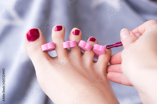 woman foot pedicure at home in progress with nail separators and red nail polish
