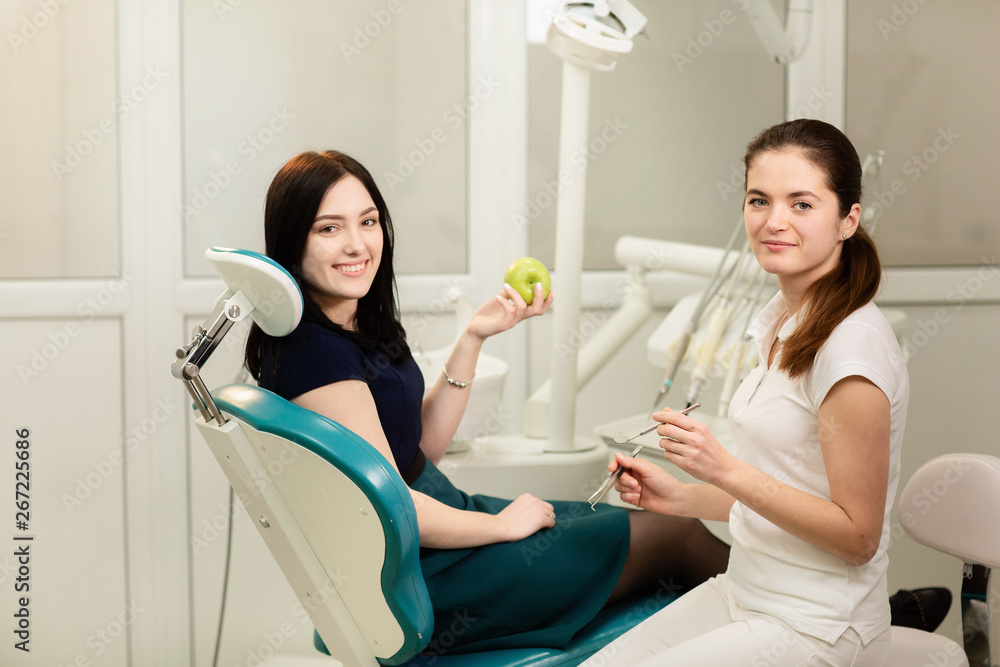 Beautiful woman patient having dental treatment at dentist's office. Smiling woman holds an apple
