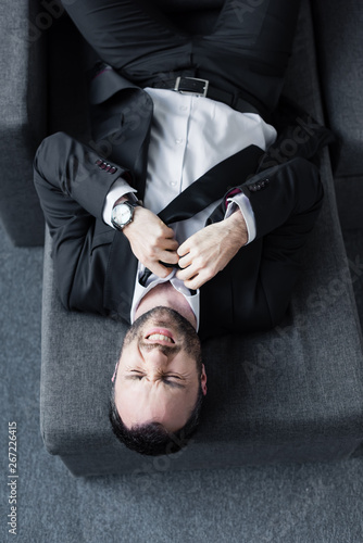 top view of depressed businessman untying tie while lying on sofa