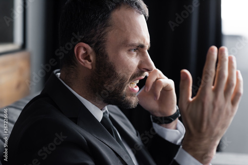 irritated businessman screaming while talking on smartphone in office