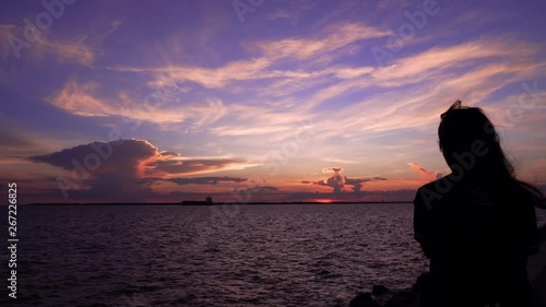 Woman sitting looking at sunset sky at sea beach . Woman silhouette backside view watches evening ocean waves enjoying wind at her face thinking dreaming