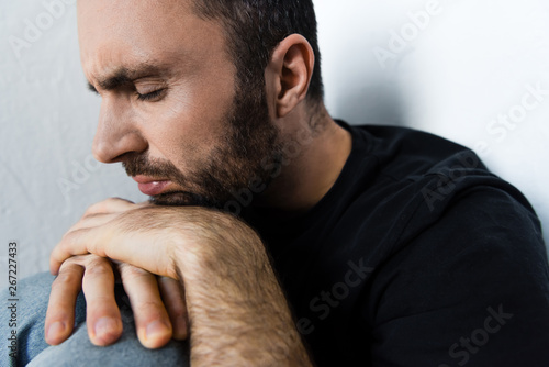 adult depressed man suffering while sitting by white wall with closed eyes