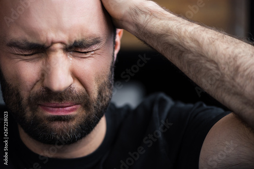 Valokuvatapetti depressed bearded man crying with closed eyes and holding hand on head