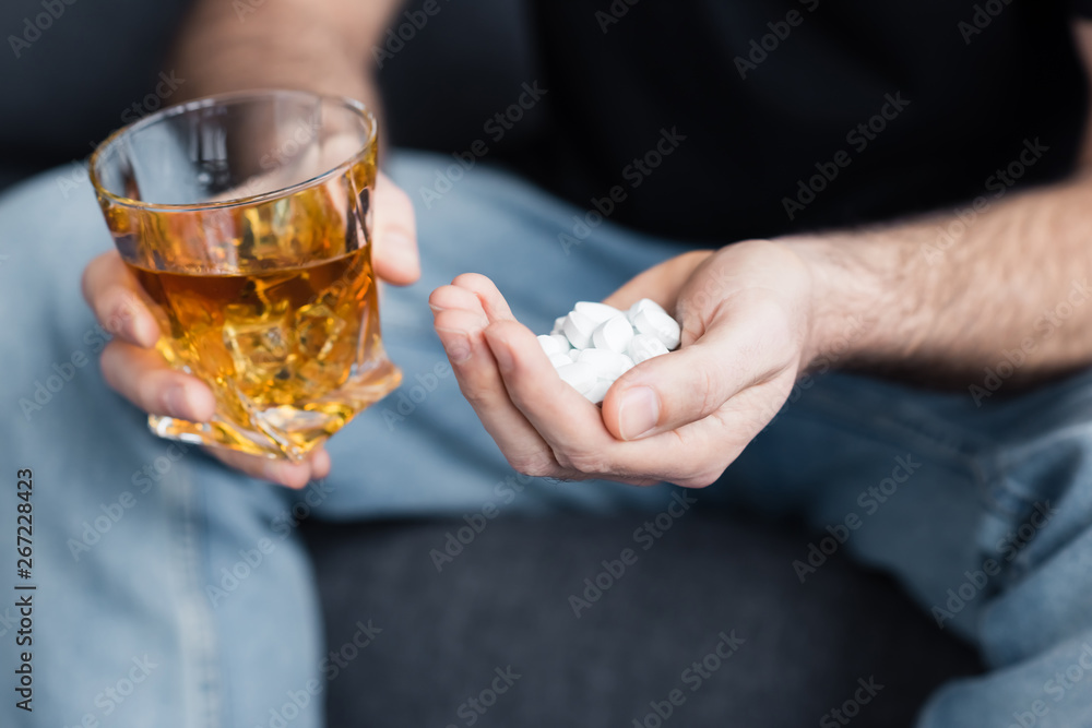 cropped view of sitting man with handful of pills and glass of whiskey cropped view of sitting man with handful of pills and glass of whiskey