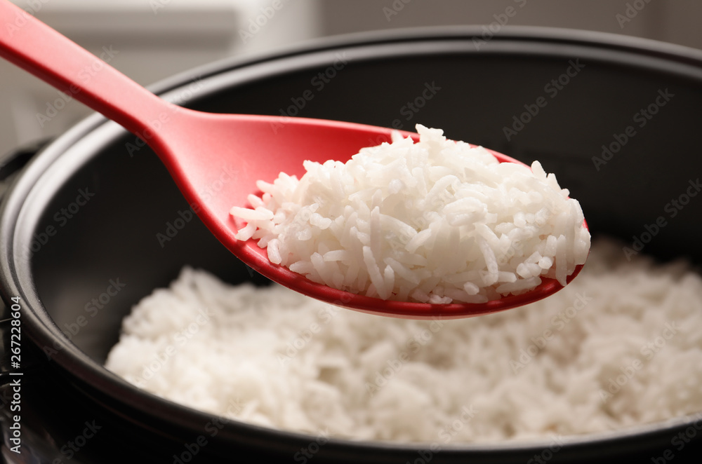Spoon with tasty hot rice over cooker, closeup Spoon with tasty hot rice over cooker, closeup