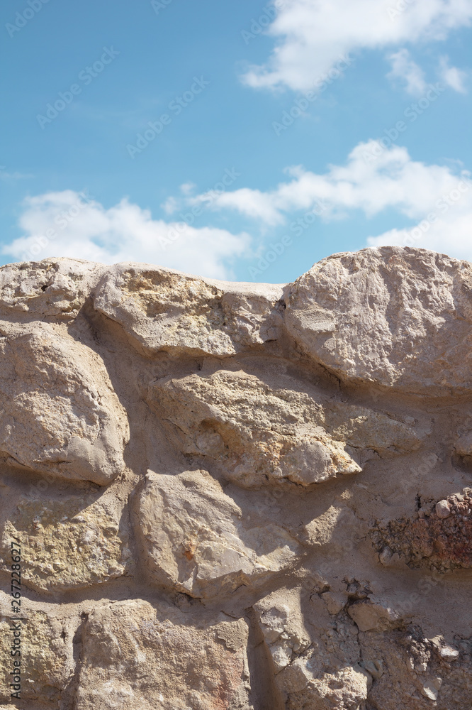 Wall made of stone and rock / Blue sky with white clouds. Warm filter and muted black