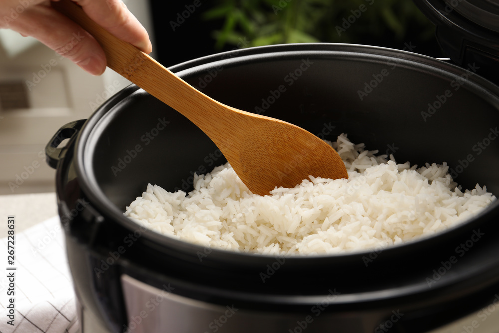 Woman taking tasty rice with spoon from cooker in kitchen, closeup