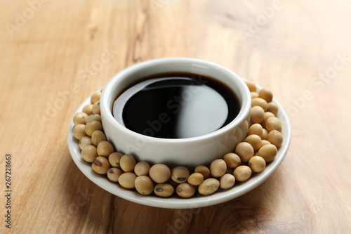 Dish of soy sauce with beans on wooden background