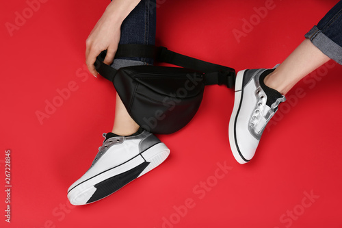 Woman in stylish shoes with bum bag sitting on color background photo