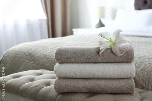 Stack of fresh towels with flower on soft bench in bedroom. Space for text