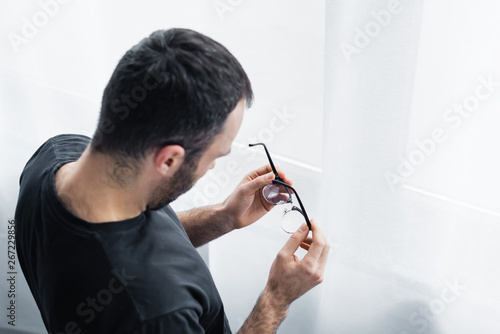 overhead view of lonely man holding glasses while standing by window at home