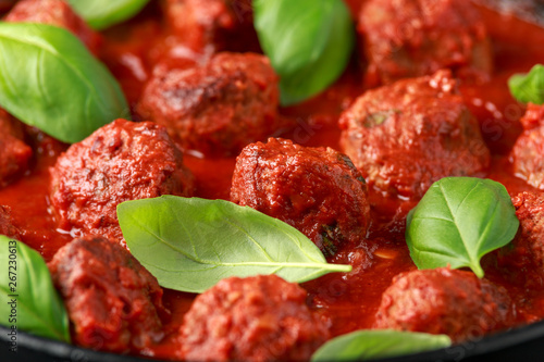 Homemade Meatballs in iron cast with sweet and hot tomato sauce, basil. On wooden table