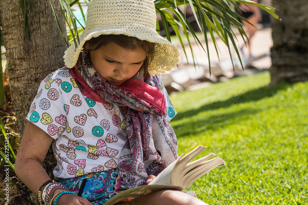 Podczas wakacji dziewczynka czyta ciekawą książkę w cieniu drzew - obrazy, fototapety, plakaty 