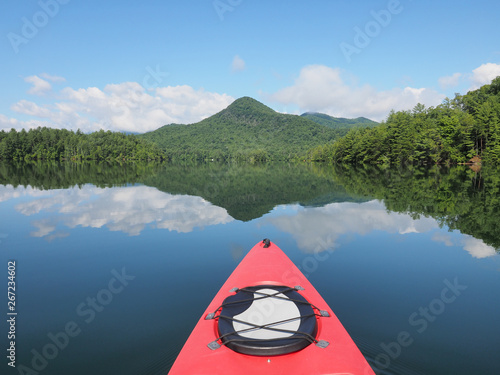 Red kayak on a beautiful summer morning in Lake Santeetlah, North Carolina, with forested hills reflected in perfectly calm water in the background.