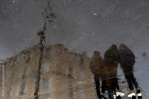 des passants se reflètent sur le béton mouillé par la pluie photo