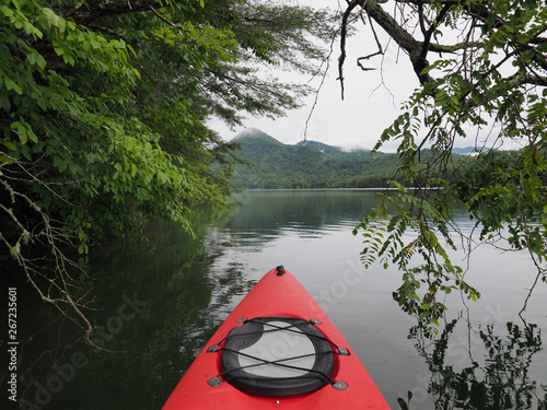 Red kayak on Lake Santeetlah, North Carolina, amidst the trees of the lakeshore with forested mountains in the background.