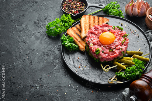 Beef steak tartare with raw egg yolk, pickled cucumber and onions. French cuisine. Top view. Free space for your text.