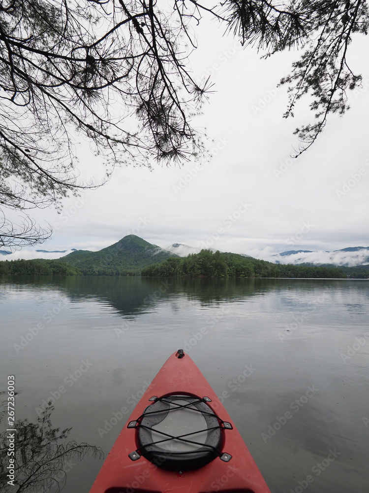 Red kayak on Lake Santeetlah, North Carolina, amidst the trees of the lakeshore with forested mountains in the background.