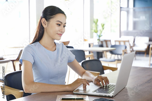 Asian pretty attractive woman working on laptop computer in coffee show with bright optimistic background