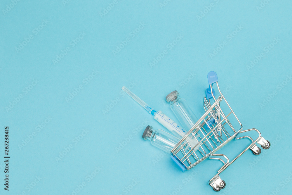 Medical injection in shopping trolley on blue background. Creative idea for health care cost, drugstore, health insurance and pharmaceutical company business concept. Copy space Medical injection in shopping trolley on blue background. Creative idea for health care cost, drugstore, health insurance and pharmaceutical company business concept. Copy space
