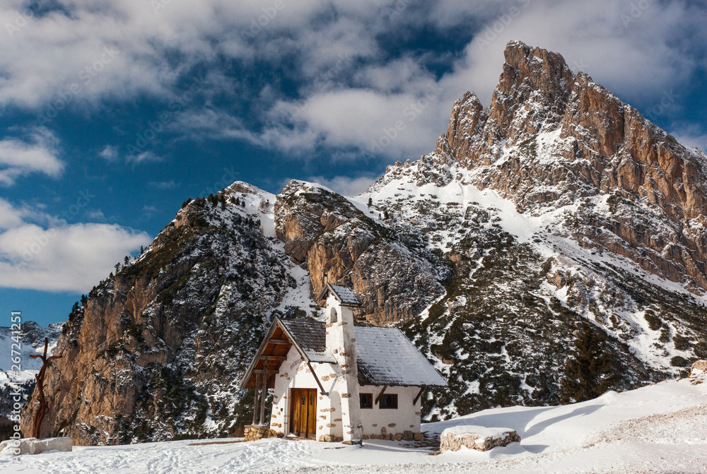 A Church with massive Mountains of the Italian Dolomites in the Background on a sunny Winter Day with blue Sky
