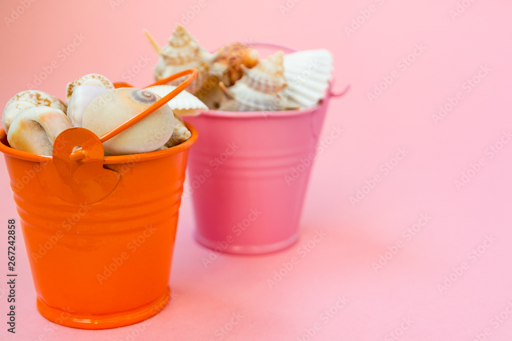 Two buckets filled with seashells on a pink background. Orange and pink bucket. There is a place for text. Maritime concept. Two buckets filled with seashells on a pink background. Orange and pink bucket. There is a place for text. Maritime concept.