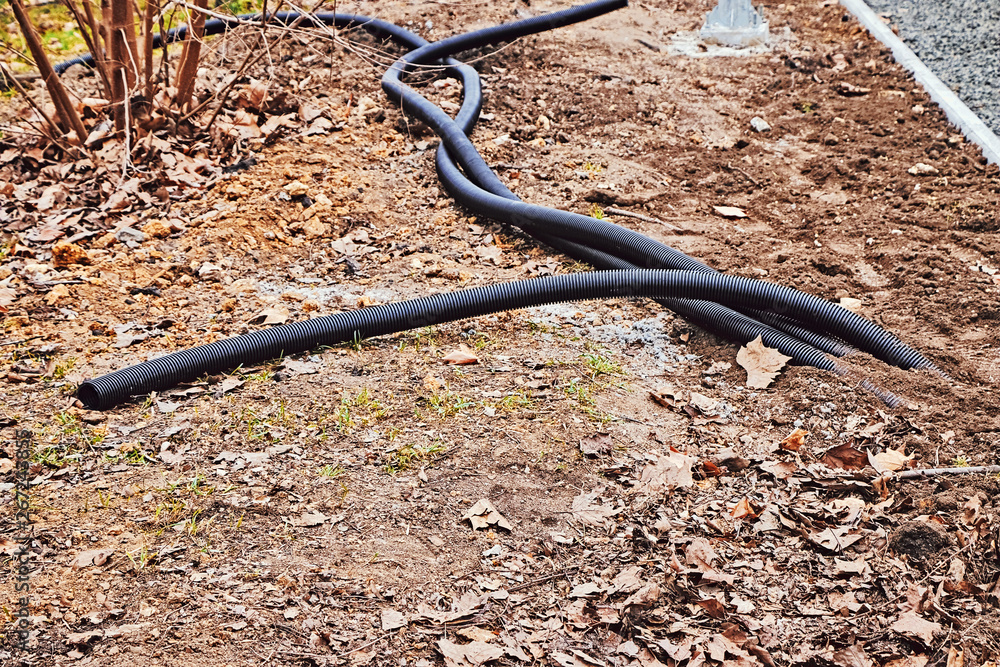 Three long black corrugated tubes lie on the ground in the park for making the connection. Three long black corrugated tubes lie on the ground in the park for making the connection.