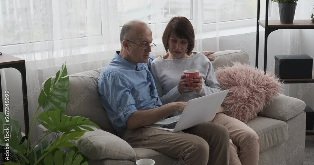 Elderly couple sitting on couch with laptop and coffee Elderly couple sitting on couch with laptop and coffee