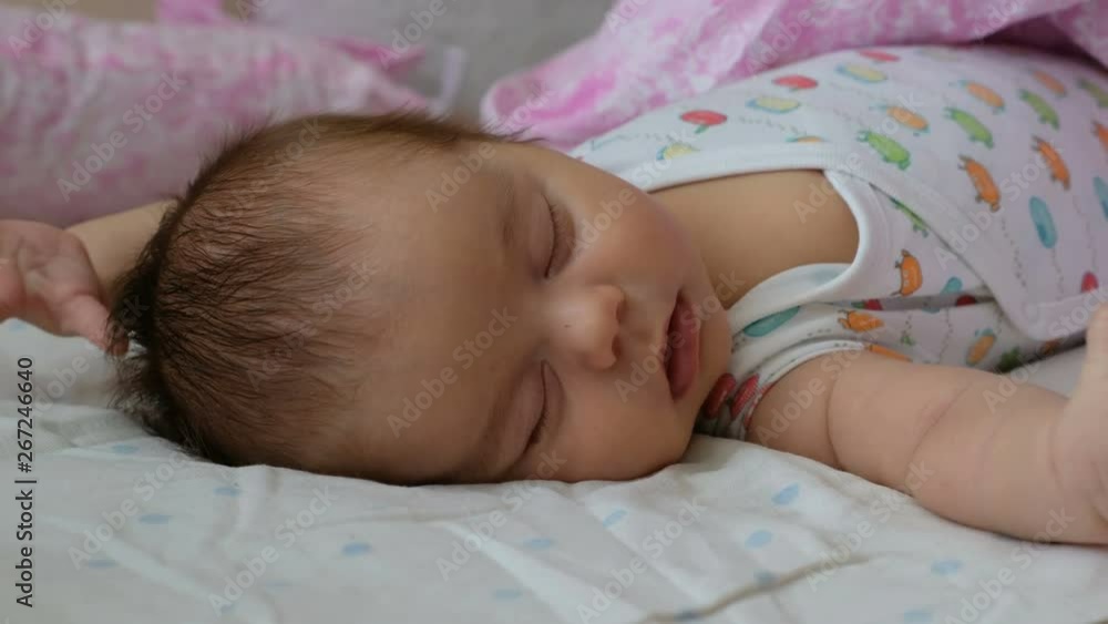 Newborn baby sleeping on a bed and flinching. Reflex moro newborns