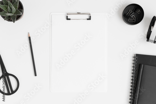 Top view of a white clipboard mockup with a succulent plant and workspace accessories on a white table.