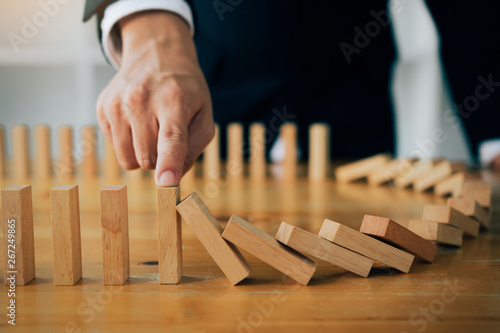 Obraz na plátně Close up finger businessman stopping wooden block from falling in the line of domino with risk concept